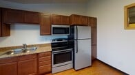Located at 1515 11th Ave N in Fargo, North Dakota, this single-floor unit offers a practical and well-appointed layout designed for comfortable everyday living. The open living area features rich, dark hardwood-style flooring, bright white walls, and natural light flowing in through multiple windows with blinds. Baseboard heating and a wall-mounted air conditioning unit ensure year-round climate control.

The kitchen is efficiently designed and fully equipped with warm wood cabinetry extending to the ceiling for ample storage, granite-style countertops, and a suite of stainless steel appliances including a refrigerator, electric range, over-the-range microwave, and dishwasher. A pass-through window connects the kitchen to an adjacent area, adding an open feel to the layout. Light wood-style flooring carries throughout the kitchen and living spaces.

The bedroom offers plush carpeting underfoot, a ceiling fan with integrated lighting, and a window that provides natural light and ventilation. A full bathroom includes a vanity with a single sink, wood-toned cabinetry with mirrored storage, tile flooring, and a bathtub. The unit also features the added convenience of an in-unit stacked washer and dryer. Overall, the space presents a clean, functional, and move-in-ready environment.