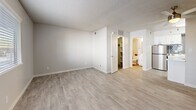 Located at 5555 E 14th St in Tucson, Arizona, this single-floor unit offers a well-organized layout comprising a living room, kitchen, bathroom, and closet. The living area is finished with light wood-look flooring throughout and features a textured ceiling with a ceiling fan, neutral-toned walls, and a front entry door flanked by a window fitted with horizontal blinds that allow natural light to filter in. The open-plan design connects the living space directly to the kitchen, which is outfitted with white shaker-style cabinetry, white countertops, a stainless steel refrigerator, and a gray subway tile backsplash that adds a modern touch. A kitchen island provides additional prep and counter space. The bathroom includes a full tub-shower combination, a white vanity with sink, and coordinating fixtures. The dedicated closet features a full-width hanging rod and upper shelf, providing practical storage. Consistent light wood-look flooring runs throughout the unit, contributing to a cohesive and clean aesthetic. The neutral color palette and updated finishes give the space a fresh, move-in-ready feel suited for comfortable everyday living in the heart of Tucson.