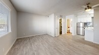 Located at 5555 E 14th St in Tucson, Arizona, this single-floor unit offers a well-organized layout comprising a living room, kitchen, bathroom, and closet. The living area is finished with light wood-look flooring throughout and features a textured ceiling with a ceiling fan, neutral-toned walls, and a front entry door flanked by a window fitted with horizontal blinds that allow natural light to filter in. The open-plan design connects the living space directly to the kitchen, which is outfitted with white shaker-style cabinetry, white countertops, a stainless steel refrigerator, and a gray subway tile backsplash that adds a modern touch. A kitchen island provides additional prep and counter space. The bathroom includes a full tub-shower combination, a white vanity with sink, and coordinating fixtures. The dedicated closet features a full-width hanging rod and upper shelf, providing practical storage. Consistent light wood-look flooring runs throughout the unit, contributing to a cohesive and clean aesthetic. The neutral color palette and updated finishes give the space a fresh, move-in-ready feel suited for comfortable everyday living in the heart of Tucson.