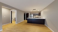 Located at 8041 W Bluemound Rd in Milwaukee, this single-floor unit showcases a contemporary design with a cohesive neutral color palette and light-toned hardwood-style flooring throughout the main living areas. The open-concept layout connects the living space directly to the kitchen, which features a large dark-cabinetry island with a crisp white countertop, pendant lighting overhead, and a suite of stainless steel appliances including a refrigerator, range, and over-the-range microwave. Dark espresso-toned cabinetry with brushed hardware lines the kitchen walls, providing ample storage alongside generous counter space.

The living area extends toward a sliding glass door that opens to a private balcony, allowing natural light to flow into the space. A dedicated bedroom offers plush carpeting, a ceiling fan, and a large window that further enhances the sense of openness and light.

The bathroom is finished with matching dark cabinetry, a grey countertop vanity, a large mirror, and the same light hardwood-style flooring found throughout the unit. A separate laundry area houses a stacked Whirlpool washer and dryer, adding practical convenience. Overall, the space presents a clean, modern aesthetic well-suited for comfortable everyday living.
