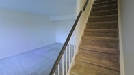 Located at 70 Old Dublin Pike in Doylestown, Pennsylvania, this two-story space offers a functional and straightforward layout across two connected levels. The interior is finished with wall-to-wall carpeting throughout, providing a comfortable and cohesive feel underfoot. A centrally positioned staircase with white balusters and a dark handrail serves as the primary connection between the two floors, lending a classic and clean aesthetic to the transition between levels. The stair treads are carpeted in a neutral tone, consistent with the rest of the interior flooring. The walls are painted in a light, neutral color palette, creating a bright and open atmosphere that allows natural light to reflect throughout the space. The lower level features open floor space with clean lines and a simple, uncluttered design that offers flexibility for a variety of uses. The overall ambiance is calm and understated, with a move-in-ready condition that makes it easy to envision a range of configurations. Situated in Doylestown, a vibrant and historically rich borough in Bucks County, this space benefits from a desirable location with access to local amenities, dining, and cultural attractions.