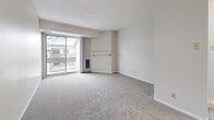 This 1-bedroom, 1-bathroom unit is thoughtfully organized across a single floor, offering a functional and comfortable layout. The living room is the largest area of the unit, featuring soft wall-to-wall carpeting, neutral light grey walls, and a textured ceiling. A standout feature is the large sliding glass door that opens to a balcony, flooding the space with natural light and providing views of the surrounding area. A wall-mounted fireplace mantel adds a subtle architectural detail to the room. The kitchen is efficiently designed with grey shaker-style cabinetry, light countertops, a white electric range, and light wood-look flooring. A window above the counter brings in additional natural light. The bedroom is a well-proportioned private retreat, also finished with plush carpeting, neutral walls, and a textured ceiling. It features a large sliding wood-panel closet that provides generous storage, and a window overlooking the exterior. The bathroom is clean and functional, with tile-surround tub and shower combination, light wood-look flooring, and white fixtures. Throughout the unit, a consistent neutral color palette and soft finishes create a calm, move-in-ready environment.