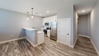 Located at 1230 Elm St, Unit 318 in Manchester, NH, this two-bedroom, one-bathroom unit offers a well-designed single-level layout with a clean, contemporary aesthetic. The open kitchen serves as the heart of the space, featuring white shaker-style cabinetry, white quartz countertops, a peninsula with a undermount sink, stainless steel appliances including a French door refrigerator, electric range, and microwave, plus pendant lighting overhead. Wood-look luxury vinyl plank flooring runs throughout the main living and kitchen areas, adding warmth and durability. Both bedrooms are finished with patterned carpet and neutral light gray walls, creating a calm and functional atmosphere. One bedroom features a narrow horizontal window that allows for natural light while maintaining privacy, along with recessed lighting. The full bathroom is appointed with wood-look flooring, a full-size soaking tub and shower combo, and matte black hardware and fixtures for a modern touch. A hallway connects the main living area to the bedrooms and bathroom, providing a logical and efficient flow throughout the unit. Clean white trim, recessed lighting, and a consistent gray color palette give the entire space a cohesive, move-in-ready feel.