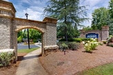 Located at 138 Greison Trail in Newnan, Georgia, The Jackson at Greison Trail makes a strong first impression with its stately stone archway entrance, a defining architectural feature that sets the tone for the entire property. The entrance is flanked by mature trees, manicured shrubs, and colorful seasonal plantings, creating a lush, welcoming approach. Classic lamp posts line the walkways and roadways, adding a timeless character to the grounds.

The property features well-paved internal roadways with clearly marked crosswalks and pedestrian sidewalks that wind through the landscaped grounds. Parking areas are thoughtfully integrated into the site, bordered by ornamental trees, flowering plants, and mulched beds that soften the hardscape. A brick monument sign prominently displays The Jackson branding near the main entrance, reinforcing the community's identity.

Towering pines and deciduous trees provide a generous canopy throughout the grounds, offering shade and a sense of established, natural surroundings. The overall ambiance is one of a carefully curated, park-like setting that balances accessibility with aesthetic appeal. The single-level layout of the site contributes to ease of navigation, while the verdant landscaping throughout ensures a consistently inviting atmosphere for all who arrive.