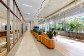 Located at 50 Western Avenue in Boston's Allston neighborhood, this generously proportioned amenity floor spans a single level and offers a diverse range of spaces designed for work, recreation, and relaxation. The entry lobby makes an immediate impression with its curved wood-paneled reception desk, fluted wall cladding, polished terrazzo flooring, and recessed lighting that sets a warm, refined tone. A sweeping central corridor connects the various zones, lined with glass-partitioned offices that allow natural light to flow throughout. The open coworking lounge is a standout feature, showcasing floor-to-ceiling windows overlooking lush greenery, sculptural wood planter dividers, pendant lighting, exposed concrete ceilings, and flexible seating for both collaborative and individual work. A bright, airy dining area complements the workspace with light wood flooring and generous daylighting. Recreation amenities include a billiards room with bold geometric tilework and patterned wallcoverings, a dedicated golf simulator room with dark walls and turf flooring, and a plush private screening room wrapped in deep blue textured panels with a large-format display. The fitness center is well-equipped with professional-grade machines, mint-toned walls, circular halo lighting, and full-length mirrors, completing this thoughtfully designed, amenity-rich environment.