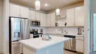 Located on Park Lane in Davenport, Florida, this single-story unit offers a clean, contemporary design with a cohesive neutral color palette throughout. Light wood-look plank flooring extends across the entire space, contributing to a bright and airy atmosphere.

The kitchen serves as a central highlight, featuring crisp cream cabinetry with brushed nickel hardware, a classic white subway tile backsplash, and light quartz countertops. A center island provides additional prep space and is illuminated by modern cylindrical pendant lights. Stainless steel appliances — including a French door refrigerator, range, microwave, and dishwasher — complete the functional layout. Open shelving adds a decorative touch alongside ample cabinet storage.

The bedrooms are generously sized, each featuring ceiling fans, natural light from multiple windows with blinds, and a calm, neutral finish on the walls. The primary bathroom includes a glass-enclosed walk-in shower, dual-sink vanity with light cabinetry, and direct access to a spacious walk-in closet outfitted with wire shelving systems.

A dedicated laundry area houses a stacked full-size washer and dryer, adding everyday convenience to this well-designed space.
