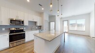 Located at 1000 Everly Way in Gainesville, Georgia, this single-floor residence showcases a clean, contemporary design with a cohesive color palette of whites and warm wood tones throughout. The open-concept kitchen serves as the heart of the home, anchored by a substantial granite-topped island with elegant pendant lighting overhead. White shaker-style cabinetry lines the walls, complemented by a soft gray subway tile backsplash and a full suite of stainless steel appliances, including a French door refrigerator, range, microwave, and dishwasher. Wood-look flooring flows seamlessly from the kitchen into the adjoining living area, which is bathed in natural light from large windows with blinds and offers access to an outdoor area. The bedrooms are well-proportioned, each featuring the same warm hardwood-style flooring and bright windows. The primary bathroom includes a granite-topped vanity with white cabinetry, a glass-enclosed shower, and direct access to a generously sized walk-in closet with built-in shelving rods. A secondary bathroom features a soaking tub with a tiled surround and a matching vanity. Throughout the space, high ceilings and recessed lighting contribute to an airy, bright ambiance.
