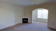 This single-floor residence offers a comfortable and well-designed layout with a warm, neutral aesthetic throughout. The living area serves as the heart of the home, anchored by a classic fireplace with a clean white mantel that provides a natural focal point for the room. Soft, wall-to-wall carpeting in a neutral tone runs throughout, adding warmth underfoot and contributing to the overall inviting atmosphere.

A standout architectural detail is the graceful arched entryway that connects the living space to an adjacent area, lending the home a sense of character and openness. Large windows flood the space with generous natural light, enhancing the airy feel of the rooms and offering views of the surrounding greenery outdoors.

The interior is finished with smooth, light-colored walls and white trim, creating a clean and versatile backdrop that suits a variety of furnishing styles. The ceiling is well-proportioned, contributing to an open and uncluttered feel. Ventilation is supported by a ceiling-integrated vent, reflecting thoughtful functional design. Overall, this home presents a bright, move-in-ready space with timeless architectural touches and a layout that balances comfort with practicality.