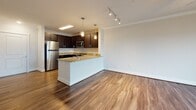 Located at 2150 Bond St. in Charlottesville, Virginia, this well-appointed single-floor residence offers a thoughtfully designed layout with modern finishes throughout. The open-concept kitchen serves as a central highlight, featuring rich dark cabinetry, granite countertops, stainless steel appliances including a refrigerator, range, and over-the-range microwave, and elegant pendant lighting over a peninsula — ideal for both cooking and casual dining.

The living area flows seamlessly from the kitchen and is finished with gleaming hardwood-style flooring, crown molding, and a ceiling fan. A sliding glass door opens to a private balcony, allowing for natural light and outdoor views that enhance the overall sense of openness.

The bedroom is generously proportioned with plush carpeting and a well-positioned window that brings in natural light. The hallway leading to the bedroom provides practical utility, with access to closets and a full bathroom. The bathroom is finished with hardwood-style flooring, a granite-topped dark vanity, and a full shower-tub combination with tiled surround.

Throughout the residence, a neutral color palette, clean lines, and quality materials create a cohesive and inviting atmosphere, making this Charlottesville property a comfortable and stylish place to call home.