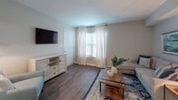 This single-floor residence offers a thoughtfully designed layout that balances comfort and functionality across its key living spaces. The living room serves as the heart of the home, featuring warm-toned hardwood-style flooring, neutral gray walls, and a bright window dressed with sheer white curtains and plantation shutters that allow natural light to fill the room. The open-concept kitchen is positioned adjacent to the living area and is outfitted with warm honey-toned wood cabinetry, light granite-style countertops, and black appliances including a gas range, dishwasher, and full-size refrigerator. Ample upper and lower cabinet storage, combined with a flush-mount ceiling light, make this a practical and well-lit workspace. The bedroom is a serene retreat, finished with the same hardwood-style flooring, soft neutral walls, and a ceiling fan with light fixture overhead. A window with patterned curtains provides natural light while maintaining privacy. The bathroom features a tub-shower combination with a curtained enclosure, a toilet, and clean white fixtures set against neutral walls. Throughout the residence, the consistent use of neutral tones, durable flooring, and natural light creates a cohesive, inviting ambiance.