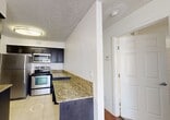 This compact yet well-designed 500 square foot apartment in Boca Raton, Florida, offers a harmonious blend of functionality and style. The single-floor layout comprises one bedroom, one bathroom, and an open-concept living area. The 140 square foot primary bedroom features plush carpeting and a ceiling fan, providing comfort and air circulation. The living room boasts sleek hardwood flooring and ample natural light through a large window, creating an inviting atmosphere. The kitchen is a standout feature with its modern stainless steel appliances, dark wood cabinetry, and elegant granite countertops. A convenient in-unit laundry area adds to the apartment's practicality. The bathroom, though modest, is well-appointed with a tub-shower combination and clean, white tiling. Throughout the space, neutral wall colors and textured ceilings contribute to a bright, airy feel. The apartment also offers outdoor access via a glass door, hinting at potential exterior views or a small private outdoor area. Despite its compact size, this apartment efficiently utilizes space to create a comfortable and stylish living environment.