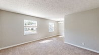Located at 1512 E 10th St in Jeffersonville, Indiana, this one-bedroom, one-bathroom unit offers a practical and comfortable single-floor layout. The living area features neutral gray walls and plush wall-to-wall carpeting, creating a warm and inviting atmosphere with easy access to the kitchen. The kitchen is efficiently designed with white cabinetry, granite-look countertops, a stainless steel electric range, and black refrigerator, all set atop wood-look vinyl flooring. A skylight-style ceiling fixture brightens the galley-style space. The hallway connects the rooms seamlessly, maintaining a logical and functional flow throughout. The bedroom is a well-proportioned retreat with soft carpeting, a textured ceiling, and a window that allows natural light and outdoor views to fill the room. The bathroom is tastefully finished with wood-look flooring, a white vanity topped with granite countertops, a large mirror with stylish lighting, and a full tub/shower combo. Grab bars are conveniently installed, adding a practical safety feature. Throughout the unit, consistent gray tones and clean white trim create a cohesive, modern aesthetic that is both understated and welcoming.