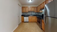 Located at 135 Ward St in Revere, Massachusetts, this single-floor unit offers a well-organized layout with distinct living, sleeping, and functional spaces. The kitchen is equipped with warm honey-toned wood cabinetry, dark granite countertops, a mosaic tile backsplash, and stainless steel appliances including a refrigerator, electric range, and dishwasher. Tile flooring runs throughout the kitchen and dining area, providing a clean and durable surface. The open living area transitions seamlessly from the kitchen and features plush wall-to-wall carpeting, baseboard heating, a wall-mounted air conditioning unit, and a large sliding glass door that invites natural light and provides access to the outdoors. Additional carpeted rooms serve as generously sized bedrooms, each featuring neutral walls, baseboard heating, and windows fitted with vertical blinds that allow for natural light and privacy. The full bathroom includes tile flooring, a standard toilet, and a bathtub with a shower curtain rod. Throughout the unit, the clean white walls, consistent flooring transitions, and practical fixtures contribute to a bright, functional, and move-in-ready atmosphere.