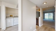 This two-story residence is thoughtfully organized across two floors, with the main living areas on the ground floor and bedrooms on the upper level. The ground floor houses the entrance, a living room with sliding glass doors fitted with vertical blinds that allow ample natural light, and a kitchen equipped with stainless steel appliances including an electric range with over-the-range microwave, granite-style countertops, and white cabinetry. A dedicated laundry area with a full-size washer and dryer is conveniently located on this level. Light wood-style flooring runs throughout the main floor, contributing to a clean, cohesive aesthetic. A staircase connects the two levels, leading to the upper floor where both bedrooms are found. The carpeted bedrooms feature neutral wall tones and window treatments that admit natural light. The primary bedroom offers a comfortable footprint with closet access. Three bathrooms are distributed throughout the home; one features a walk-in shower with sliding glass doors, while another includes a full soaking tub. All bathrooms include white cabinetry with granite-style countertops and light wood-style flooring, maintaining a consistent finish throughout the residence.