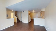 This two-story residence offers a practical and welcoming layout designed for comfortable everyday living. The main floor showcases an open-concept design that seamlessly connects the living area to the kitchen, creating a spacious and airy atmosphere. Rich, dark hardwood-style flooring runs throughout the main level, adding warmth and visual continuity to the space.

The kitchen is well-equipped with essential appliances including a refrigerator and range, and features wood-toned cabinetry that provides ample storage. A raised counter with an attached breakfast bar serves as a natural divider between the kitchen and living areas while maintaining the open feel of the floor plan. Recessed and flush-mount ceiling lighting illuminates the space effectively throughout.

Warm beige-toned walls complement the flooring and cabinetry, contributing to a cohesive and neutral interior palette. A staircase with carpeted treads leads to the second floor, where additional living space is found. The textured ceiling throughout the main level adds a subtle architectural detail. A central hallway connects the kitchen zone to the rest of the main floor, with a thermostat conveniently positioned on the wall. Overall, the space offers a clean, functional design with a straightforward and efficient floor plan suited for a variety of lifestyles.