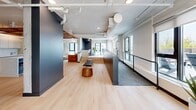Located at 575 Princess Street in Kingston, Ontario, this thoughtfully designed amenity space offers a generous, open-plan layout spread across a single floor. The interior showcases a contemporary aesthetic, combining light hardwood flooring with bold navy accent walls, exposed white ductwork, and concrete structural elements that lend an industrial-modern character to the space.

The open layout is divided into distinct functional zones that flow seamlessly into one another. A lounge area features a plush caramel velvet sofa set against a dramatic dark accent wall, creating a warm and inviting gathering spot. Nearby, a bar and kitchen area stands out with a striking rust-toned perforated ceiling panel overhead, a blue island with terracotta bar stools, and built-in appliances alongside sleek cabinetry. A dedicated dining area accommodates a wood communal table with leather chairs, lit by a pendant fixture above.

Large windows throughout invite abundant natural light, while a split-level layout with steps adds architectural interest. The space also features a carpeted corridor zone and ample room for circulation.

Extending outdoors, the rooftop terrace is a standout feature, offering an expansive tiled patio with Adirondack seating, raised planter beds filled with lush greenery, accessible ramps, and open sky views — ideal for outdoor gatherings and relaxation.