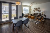 Located at 1040 Ebenezer Rd in Knoxville, TN, this well-appointed single-floor unit offers a thoughtfully designed layout that balances modern style with everyday functionality. The open-concept kitchen serves as a central highlight, featuring crisp white shaker cabinetry, quartz countertops, a central island with pendant lighting overhead, and a full suite of stainless steel appliances including a refrigerator with ice maker, electric range, microwave, and dishwasher. Rich wood-look flooring runs throughout the main living and kitchen areas, adding warmth and continuity. The living room is bright and inviting, with large windows that bring in generous natural light and a ceiling fan overhead. A private balcony access is also visible from the living area. The primary bedroom includes a ceiling fan, carpet flooring, and direct access to an en-suite bathroom. The bathrooms are finished with white cabinetry, quartz-style countertops, and tub-shower combinations. A secondary bedroom features large windows with outdoor views and access to a closet, making it well-suited as a guest room or home office. The unit's clean, neutral color palette and modern finishes throughout create a cohesive and comfortable living environment in a convenient Knoxville location.