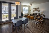 Located at 1040 Ebenezer Rd in Knoxville, TN, this well-appointed single-floor unit offers a thoughtfully designed layout that balances modern style with everyday functionality. The open-concept kitchen serves as a central highlight, featuring crisp white shaker cabinetry, quartz countertops, a central island with pendant lighting overhead, and a full suite of stainless steel appliances including a refrigerator with ice maker, electric range, microwave, and dishwasher. Rich wood-look flooring runs throughout the main living and kitchen areas, adding warmth and continuity. The living room is bright and inviting, with large windows that bring in generous natural light and a ceiling fan overhead. A private balcony access is also visible from the living area. The primary bedroom includes a ceiling fan, carpet flooring, and direct access to an en-suite bathroom. The bathrooms are finished with white cabinetry, quartz-style countertops, and tub-shower combinations. A secondary bedroom features large windows with outdoor views and access to a closet, making it well-suited as a guest room or home office. The unit's clean, neutral color palette and modern finishes throughout create a cohesive and comfortable living environment in a convenient Knoxville location.