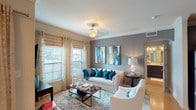 This single-floor residence is thoughtfully designed with a cohesive neutral and gray color palette accented by teal and warm tones throughout. The living room serves as the central gathering space, featuring crown molding, an elegant ceiling fixture, and large windows dressed with layered roman shades and sheer curtains that allow natural light to filter in. A gray accent wall provides a backdrop for decorative artwork, while plush seating arranged around a wooden coffee table creates an inviting atmosphere.

The kitchen is well-equipped with dark espresso cabinetry, stainless steel appliances including a range, microwave, and dishwasher, complemented by light stone countertops and a classic white subway tile backsplash. Under-cabinet lighting enhances functionality, and a built-in desk nook with open shelving offers additional utility.

Two bedrooms feature carpeted floors, ceiling fans, and soft gray accent walls. The primary bedroom includes a private ensuite bath, while a shared full bathroom with dark cabinetry and a wide vanity serves the second bedroom. A dedicated laundry room houses a full-size washer and dryer. The dining area features sliding glass doors opening to an outdoor space, bringing natural light into the room.