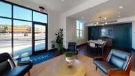 Located at 566–574 El Camino Real in San Carlos, California, this single-story commercial space offers a thoughtfully designed interior that balances modern aesthetics with a warm, inviting atmosphere. The space is anchored by a street-facing lounge area with floor-to-ceiling black-framed glass doors and windows that flood the interior with natural light while providing direct views of El Camino Real. Dark hardwood flooring runs throughout, providing a rich contrast to the crisp white walls and teal accent elements that define the space's color palette.

The lounge area near the entrance features leather seating, a woven area rug, and potted greenery, creating a relaxed yet polished welcome zone. A branded entry mat reinforces the space's identity as a Prometheus property. Moving deeper into the interior, the space transitions into a dining and meeting area appointed with a marble-top table, upholstered chairs, and a sculptural multi-bulb pendant light fixture. A dedicated booth seating alcove with teal-upholstered banquettes, terracotta barrel chairs, brass wall sconces, and pendant lighting offers an intimate setting. A restroom is accessible from the main floor, marked with a teal door consistent with the space's design language.
