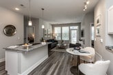 This single-floor residence offers a thoughtfully designed open-concept layout that seamlessly connects the kitchen, dining, and living areas. The living room is anchored by large windows and a glass-paneled door that invite abundant natural light and provide outdoor views, complemented by wood-style flooring and a textured ceiling throughout the main living areas.

The kitchen is well-equipped with white shaker cabinetry, granite countertops, a bold navy tile backsplash, stainless steel appliances including a side-by-side refrigerator, built-in microwave, and dishwasher. A peninsula with a granite overhang provides additional workspace and casual seating. A built-in wine rack adds a distinctive detail.

The bedrooms feature plush carpeting, generous window coverage for natural light, and ceiling fans. The primary bedroom connects directly to a full bathroom finished with granite vanity counters, wood-style flooring, and a glass-enclosed tub and shower combination. A dedicated walk-in closet with multi-level hanging rods and shelving provides substantial storage. A second full bathroom mirrors similar finishes, maintaining design consistency throughout the residence.