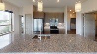 This single-floor residence presents a thoughtfully designed layout with contemporary finishes and a cohesive modern aesthetic. The kitchen serves as a central highlight, featuring rich wood-toned cabinetry, stainless steel appliances including a refrigerator, range, and microwave, and a substantial granite-topped island with an undermount sink. Pendant lighting above the island and recessed ceiling lights enhance the workspace, while a tile backsplash adds a refined detail. Wood-look flooring extends through the kitchen and connects seamlessly to the living area, which benefits from a bank of windows providing natural light and outdoor views, complemented by a ceiling fan overhead.

The bedrooms are clean and understated, each with wood-look flooring, neutral walls, and windows framing exterior greenery. The primary bathroom offers a walk-in glass shower clad in marble-style tile, a wood-toned vanity with a white countertop, large-format floor tile, and direct access to a walk-in closet. A secondary bathroom features a soaking tub with a curved shower rod, marble-style tile surround, and a matching vanity. Throughout the unit, neutral tones, clean lines, and consistent materials create a cohesive and contemporary living environment.