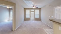 This single-floor residential unit offers a practical and comfortable layout designed for everyday living. The galley-style kitchen is well-equipped with light wood cabinetry, laminate countertops, a full suite of white appliances including a refrigerator, electric range, and dishwasher, and durable wood-look flooring. An overhead range hood and ample upper and lower cabinet storage make this kitchen both functional and efficient. The kitchen opens to the main living and dining area through a half-wall breakfast bar, creating an open, connected feel. The entryway features tile flooring and is illuminated by a chandelier-style light fixture overhead. The living room is generously proportioned, finished with wall-to-wall carpet and a ceiling fan, and benefits from natural light through large windows and a glass-paneled exterior door. The bedroom is a comfortable retreat with plush carpeting, a ceiling fan, a window with blinds for natural light, and access to a walk-in closet. The full bathroom is finished with wood-look flooring, a single-sink vanity with storage, and a tiled shower-tub combination with grab bars. Neutral wall tones and clean white trim throughout give the space a cohesive, move-in-ready aesthetic.