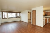 This single-floor unit offers a practical and comfortable layout designed for everyday living. The open-concept living and dining area is highlighted by warm hardwood-style flooring, a textured ceiling, a chandelier light fixture, and a large window that brings in natural light and exterior views. A wall-mounted air conditioning unit provides climate control in the living space.

The kitchen is efficiently arranged in an L-shaped configuration and features honey-toned oak cabinetry, laminate countertops, a double stainless steel sink, and a full suite of white appliances including a dishwasher, electric range, and refrigerator. An over-the-range microwave adds convenience, and recessed fluorescent lighting keeps the workspace well lit.

The bedroom is carpeted for comfort and includes a ceiling fan with light, a window overlooking the exterior, a baseboard heating unit, and a generously sized closet with built-in shelving and a sliding door. A separate dining or living area with hardwood-style flooring and an elegant chandelier provides additional flexible space.

The bathroom is clean and bright, featuring a full soaking tub with a shower surround, a vanity with stone-patterned countertop and undermount sink, and hardwood-style flooring that ties the space together with the rest of the unit's design aesthetic.