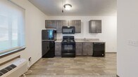 This efficiently designed single-floor unit offers a well-organized layout that makes excellent use of its intimate footprint. The open entryway transitions seamlessly between the kitchen and the main living area, with wood-look plank flooring running through the kitchen and entry zone, while plush carpet covers the living and sleeping space. An elegant chandelier hangs in the entry corridor, adding a touch of refinement to the otherwise clean, modern aesthetic.

The kitchen is outfitted with dark espresso-toned cabinetry, a light-colored countertop, and a full suite of black appliances including a refrigerator, electric range, over-the-range microwave, and dishwasher. A flush-mount ceiling light illuminates the space, keeping the kitchen bright and functional.

The main living area is spacious relative to the overall footprint, featuring soft carpet, crisp white walls, and a ceiling fan with an integrated light fixture for year-round comfort. A wall-mounted electrical panel is neatly recessed into the living area wall, and a thermostat near the entry provides climate control.

The bathroom is clean and well-appointed, featuring a full tub-shower combo with white surround, a dark-toned vanity with a marble-style countertop, and tile-look flooring. A closet provides additional storage, completing this practical and move-in-ready unit.