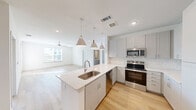 Located in Austin, TX, this well-designed single-story home offers four bedrooms, two bathrooms, and a thoughtful layout that maximizes comfort and functionality. The open-concept kitchen and living area serves as the heart of the home, featuring white shaker-style cabinetry, a subway tile backsplash, stainless steel appliances including a range, microwave, dishwasher, and refrigerator, and a central island with a stainless steel sink and pendant lighting overhead. Light wood-look flooring extends throughout the main living areas, lending a clean and cohesive aesthetic. The living room is bright and airy, benefiting from natural light and a ceiling fan. The bedrooms are carpeted and generously sized, with several rooms featuring large windows that allow abundant natural light and neighborhood views. The primary bedroom includes access to a bathroom with a white quartz vanity, tile flooring, and built-in shelving. Closets feature multi-tier shelving and hanging rods for organized storage. A dedicated laundry room houses a washer and dryer with overhead shelving. Clean white walls, recessed lighting, and a neutral color palette throughout create a bright, move-in-ready atmosphere ideal for a variety of lifestyles.
