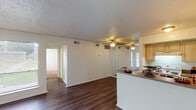 This single-story residence in Lufkin, Texas, offers a well-organized layout across two bedrooms and two bathrooms. The open-concept living and dining area serves as the central hub of the home, featuring warm wood-look laminate flooring, a ceiling fan with light fixture, and large windows that allow generous natural light to fill the space. A half-wall peninsula separates the living area from the kitchen, providing a convenient breakfast bar with granite-style countertops.

The galley-style kitchen is equipped with warm wood cabinetry, a double-basin sink, granite-style countertops, a white electric range, and a full-size refrigerator. Light tile flooring runs throughout the kitchen and entry areas, offering a clean, durable surface.

Both bedrooms feature plush carpeting and windows overlooking the outdoors, creating a calm and comfortable atmosphere. One bedroom includes access to a walk-in closet, adding practical storage. The bathrooms feature granite-style vanity countertops with wood cabinetry. Throughout the unit, a neutral white and cream color palette creates a bright, cohesive aesthetic.