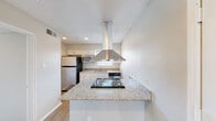 This single-story residence offers a cohesive, well-maintained interior highlighted by consistent finishes throughout. The kitchen serves as a functional centerpiece, featuring granite countertops, white shaker-style cabinetry, stainless steel appliances including a refrigerator, microwave, and dishwasher, and a peninsula with a built-in cooktop. A stainless steel range hood is suspended above, providing both a practical and visually striking element. A window above the sink allows natural light to brighten the workspace.

The living areas are finished with wood-look laminate flooring and neutral-toned walls, creating a clean, open feel. One room features vaulted ceiling lines, adding a sense of height and airiness, while another connects directly to the kitchen via an open corridor. Both spaces are well-lit through windows dressed with horizontal blinds.

The bedrooms are carpeted for comfort and each includes access to a walk-in closet with built-in racking. Ceiling fans provide additional ventilation, and windows bring in natural light. The bathroom is appointed with a granite-topped vanity, white cabinetry, a framed mirror, and a tiled tub-shower combination with chrome fixtures, completing the unit's consistent and practical design.