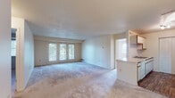 This single-floor residence offers a well-organized layout that balances open communal areas with functional private spaces. The living room is generously sized, finished with neutral wall-to-wall carpeting, and bathed in natural light through a set of three glass panel doors that open to an outdoor balcony, offering views of surrounding greenery. Adjacent to the living room, the kitchen is configured in a galley style, featuring white cabinetry with wood trim, a double sink, a dishwasher, an electric range, and a refrigerator, all set atop wood-look flooring. A pass-through counter connects the kitchen visually to the living area, creating an open and communicative flow between spaces.

The two bedrooms are carpeted and each includes an expansive wall-spanning closet outfitted with louvered bi-fold doors, providing considerable storage capacity. One bedroom benefits from its own access to a private balcony. The unit includes two bathrooms, each with wood-look flooring and light, neutral finishes. One bathroom features a tub-shower combination with grab bars, while the second offers a walk-in shower stall, also with grab bar support. Both bathrooms include a vanity with a countertop sink. Overall, the space presents a clean, practical, and well-lit environment throughout.