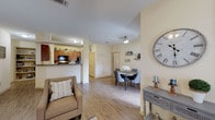 Located in Live Oak, Texas, this single-story residence offers a thoughtfully designed open-concept layout that seamlessly connects the living, dining, and kitchen areas. The living room is bright and welcoming, featuring wood-look flooring, a ceiling fan, and multiple windows dressed with sheer curtains and blinds that allow abundant natural light to fill the space. Adjacent to the living area, the dining space accommodates a round table and provides a cozy setting for everyday meals. The kitchen is well-equipped with warm wood cabinetry, granite-style countertops, a full suite of black appliances including a refrigerator, electric range, and built-in microwave, plus a double stainless steel sink and a convenient breakfast bar. A built-in shelving nook adds additional storage and display space. The two bedrooms are comfortably sized with plush carpeting, ceiling fans, and ample natural light from large windows. One bedroom features direct access to a closet and en-suite bathroom. The two bathrooms are finished with matching wood cabinetry and granite-style countertops; one includes a tiled tub-shower combination, while the other features a shower with curtain enclosure. Wood-look flooring flows throughout the main living areas, contributing to a cohesive and inviting overall ambiance.