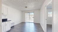 Located at 151 N Normandie Ave in Los Angeles, CA, this one-bedroom, one-bathroom unit offers a thoughtfully arranged single-floor layout that maximizes every square foot of its compact footprint. The combined kitchen and living area forms the heart of the unit, featuring dark hardwood-style flooring that runs throughout, crisp white walls, and a textured ceiling. The kitchen is well-appointed with white shaker cabinetry, dark countertops, stainless steel appliances including a gas range and refrigerator, a built-in sink, and track lighting overhead. A wall-mounted HVAC unit provides climate control. The living area benefits from a sliding glass door dressed with vertical blinds, allowing natural light to fill the space while providing access to an outdoor view. The bedroom is a well-proportioned private retreat featuring the same hardwood-style flooring, a bright window with horizontal blinds that frame neighborhood views, and a ceiling fan with a light fixture for added comfort. A dedicated closet offers convenient storage. The bathroom is finished in a clean, all-white palette with dark tile flooring, a full bathtub with an overhead rain showerhead, a white vanity with storage cabinetry, and a wall-mounted mirror. The unit's consistent, modern finishes create a cohesive and functional living environment throughout.