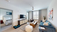 Located at 9303 Sun Bluff Way in Fredericksburg, VA, this one-bedroom, one-bathroom residence offers a well-designed layout with modern finishes across a single floor. The open-concept living and kitchen area serves as the heart of the home, bathed in natural light from large windows dressed with elegant floor-to-ceiling drape panels. The living area features light wood-style flooring and a ceiling fan, creating a comfortable and inviting atmosphere. The kitchen is outfitted with two-tone cabinetry — crisp white uppers paired with slate gray lowers — complemented by white quartz countertops, stainless steel appliances, and a spacious peninsula with bar seating, ideal for dining and entertaining. The bedroom is a serene retreat with large windows overlooking the balcony, allowing ample natural light and outdoor views. The bathroom is long and corridor-style, featuring light wood flooring, a full tub-shower combination, and a modern vanity with ample storage. A private balcony extends the living space outdoors. Five closets throughout the unit provide exceptional storage. The clean, neutral color palette and contemporary design choices lend a polished, move-in-ready feel to the entire space.