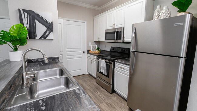 Cocine, limpie y entretenga con facilidad en esta cocina totalmente equipada, que cuenta con electrodomésticos de acero inoxidable, gabinetes blancos tipo shaker y pisos estilo madera. - Elevate 155