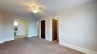 Located at 4111 Walnut Street in Philadelphia, PA, this single-floor residence combines classic architectural charm with a clean, neutral aesthetic. The interior is finished with soft gray walls and white trim throughout, creating a bright and cohesive feel. Plush wall-to-wall carpeting in a warm neutral tone adds comfort underfoot and flows seamlessly between spaces. A standout architectural detail is the elegant arched doorway, which connects rooms with a timeless, classic touch that contrasts beautifully with the more contemporary square-framed doorways elsewhere in the space. Rich dark wood doors add a bold contrast against the light walls and white trim, lending a sense of character and depth to the interior. The ceiling fan with integrated lighting provides both functional air circulation and ambient illumination. The layout features multiple doorways suggesting well-defined, connected rooms, with closet or utility access thoughtfully integrated. A wall-mounted thermostat panel indicates climate control throughout. The overall ambiance is calm and move-in ready, with a neutral palette that offers flexibility for personalization. This residence presents a solid blend of traditional Philadelphia residential architecture and practical, comfortable living.