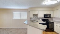 This compact yet efficiently designed single-floor unit offers a comfortable and functional living experience across its one bedroom and one bathroom layout. The open-concept kitchen and living area serves as the heart of the space, where the kitchen showcases white cabinetry, a mosaic tile backsplash, granite-style countertops, a peninsula breakfast bar, and black appliances including a range, built-in microwave, and dishwasher, complemented by a stainless steel refrigerator and wood-look flooring. The living area flows seamlessly from the kitchen and features soft carpeting and a sliding glass door that opens to a private balcony with outdoor views, filling the room with natural light. The bedroom is carpeted and includes a ceiling fan, ample wall space, and direct access to a dedicated closet with laundry facilities. The bathroom offers a full tub-shower combination with clean white tile surround and chrome fixtures. Throughout the unit, warm neutral tones on the walls and textured ceilings create a consistent, understated aesthetic. The inclusion of in-unit laundry and a private balcony adds notable everyday convenience to this well-organized living space.