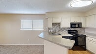 This compact yet efficiently designed single-floor unit offers a comfortable and functional living experience across its one bedroom and one bathroom layout. The open-concept kitchen and living area serves as the heart of the space, where the kitchen showcases white cabinetry, a mosaic tile backsplash, granite-style countertops, a peninsula breakfast bar, and black appliances including a range, built-in microwave, and dishwasher, complemented by a stainless steel refrigerator and wood-look flooring. The living area flows seamlessly from the kitchen and features soft carpeting and a sliding glass door that opens to a private balcony with outdoor views, filling the room with natural light. The bedroom is carpeted and includes a ceiling fan, ample wall space, and direct access to a dedicated closet with laundry facilities. The bathroom offers a full tub-shower combination with clean white tile surround and chrome fixtures. Throughout the unit, warm neutral tones on the walls and textured ceilings create a consistent, understated aesthetic. The inclusion of in-unit laundry and a private balcony adds notable everyday convenience to this well-organized living space.