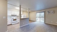 Located at 1905 W Appleway Ave in Coeur d'Alene, Idaho, this single-floor unit offers a practical and well-organized layout designed for comfortable everyday living. The open-concept living and kitchen area is defined by a partial dividing wall that separates the two spaces while maintaining an airy, connected feel. The living area features plush carpeting and a sliding glass door that opens to a private balcony, allowing natural light to filter into the space. A baseboard heating system runs along the living room wall, providing efficient warmth throughout. The kitchen is outfitted with white cabinetry, white appliances including an electric range and a full-size refrigerator, a built-in dishwasher, and a single-basin sink. Light wood-style flooring runs throughout the kitchen, complementing the neutral wall tones and textured ceiling. An in-unit washer is also present, adding everyday convenience. The bedroom is carpeted and features a window with blinds that brings in natural light, along with a generous sliding double-door closet offering ample storage. The overall aesthetic is clean and neutral, with white trim and soft beige tones creating a bright, functional living environment throughout the unit.