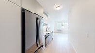 Located on SE Milwaukie Avenue in Portland, Oregon, this thoughtfully designed one-bedroom, one-bathroom unit offers a clean, modern aesthetic throughout its efficiently arranged single-floor layout. Light oak-toned hardwood flooring flows continuously through every room, complementing crisp white walls and creating a bright, cohesive atmosphere.

The kitchen runs along one wall in a galley-style configuration, outfitted with stainless steel appliances including a full-size refrigerator and range, a built-in dishwasher, white cabinetry extending to the ceiling, white subway tile backsplash, and a sleek undermount sink with a matte black faucet. The kitchen opens directly into the living area, which benefits from a large picture window framing leafy neighborhood views and allowing generous natural light to fill the space.

The bedroom is a comfortable size, featuring two windows, a built-in closet with shelving, and a wall-mounted HVAC unit. The bathroom showcases a clean, contemporary design with vertically stacked white tile in the walk-in shower, a matte black fixtures package, an undermount vanity sink, and a mirrored medicine cabinet. A dedicated laundry area houses a stacked washer and dryer unit, adding everyday convenience to this well-appointed home.