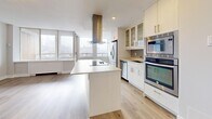 This thoughtfully designed 2-bedroom, 2-bathroom residence offers a bright and contemporary living experience across a single floor. The open-concept kitchen and living area form the heart of the space, characterized by light hardwood flooring, large windows that invite abundant natural light, and a clean, neutral color palette. The kitchen is well-equipped with a central island featuring an induction cooktop, a stainless steel overhead range hood, full-size stainless steel appliances including a double wall oven and dishwasher, and ample cabinetry with glass-front upper cabinets for display storage. The adjoining living room is generously sized and benefits from large windows with open views. The spacious primary bedroom provides a comfortable retreat, while the second bedroom also features a double closet and light-toned hardwood floors. Both bedrooms are served by elegant flush-mount light fixtures. The two bathrooms are finished with neutral stone-look tile flooring; one features a tub-shower combination with tiled surround, while the other includes a glass-enclosed shower and an extended vanity with a white countertop. A dedicated in-unit laundry room with side-by-side washer and dryer completes this well-appointed residence.