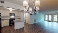 This single-floor residence offers two bedrooms and two bathrooms with a thoughtfully designed layout. The open-concept living and dining area is spacious and bright, anchored by rich hardwood-style flooring and an elegant multi-light chandelier that adds a refined focal point to the dining space. Large windows allow natural light to filter in, with outdoor greenery visible from the bedrooms.

The kitchen is well-equipped with crisp white shaker cabinetry, granite countertops, and a full suite of black appliances including a gas range, microwave, dishwasher, and refrigerator. A peninsula provides added counter space and casual seating potential. An in-unit stacked washer and dryer is conveniently accessible just off the kitchen.

Both bedrooms feature plush carpeting and generous closet space, including a walk-in closet in the primary bedroom. The primary bathroom offers a glass-enclosed walk-in shower with tile surround, granite vanity, and light tile flooring. The second bathroom includes a full soaking tub and shower combo, also finished with granite countertops and neutral tile flooring. Clean white walls and consistent finishes throughout create a cohesive, move-in-ready atmosphere.