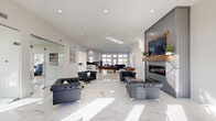 Located in the Chenal Valley area of Little Rock, Arkansas, this single-floor community space offers a sophisticated and well-appointed environment designed for both relaxation and activity. The expansive living room serves as the centerpiece, featuring gleaming white marble-style tile floors with gold veining, a wall-mounted fireplace framed by a rustic wood mantel and gray shiplap surround, and a large flat-screen TV. Tufted black leather seating with gold-accented legs is arranged throughout, complemented by a pool table and foosball table for recreation. Recessed lighting and large windows flood the space with natural light, while a decorative gold laurel emblem is inlaid into the flooring. The open kitchen is outfitted with high-gloss white cabinetry, bold black granite countertops with a matching backsplash, stainless steel appliances, and a central island with pendant lighting and gold-trimmed bar seating. The hallway features additional natural light and a planter display. The fitness room is well-equipped with treadmills, a cable machine, an elliptical, and a rowing machine, set on hardwood-style flooring with wall mirrors and expansive windows offering views of the surrounding community.