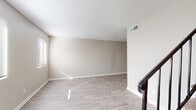 This two-story residence is designed with a clean, neutral aesthetic throughout. The main level features light wood-look flooring that extends across the open living areas, providing a cohesive and bright feel. Natural light filters in through blinded windows, illuminating the warm beige walls and white trim that are consistent throughout the home. A carpeted staircase with a dark metal railing connects the two floors, serving as a functional focal point in the entryway.

The kitchen is equipped with white cabinetry, light stone-style countertops, and black appliances including a range, dishwasher, and refrigerator. A flush-mount ceiling light and overhead ventilation keep the space practical. A half bathroom on the main level includes a single-sink vanity with a granite-style countertop, white cabinetry, and wood-look flooring.

Upstairs, the bedrooms are carpeted and feature neutral walls with natural window light. At least one bedroom includes a walk-in closet. The full bathroom on this level offers a single-sink vanity with white cabinetry, a tiled shower-tub combination, and wood-look flooring. Textured ceilings are present in several rooms, adding subtle dimension to the overall interior.