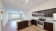 This single-story residence features a thoughtfully designed open floor plan that maximizes its generous footprint across two bedrooms and three bathrooms. Vaulted ceilings rise prominently over the main living and kitchen areas, amplifying the sense of space and allowing natural light to filter throughout the interior. Warm-toned wood-look flooring runs through the living room, kitchen, and hallways, while plush carpet provides comfort in both bedrooms.

The kitchen is a functional centerpiece of the home, equipped with dark espresso cabinetry, granite-style countertops, stainless steel appliances including a range, microwave, dishwasher, and refrigerator, and a peninsula with an integrated sink that opens directly to the living area. Pendant lighting and recessed fixtures illuminate the space efficiently.

The living room benefits from a large window that introduces natural light and is fitted with a ceiling fan. Both bedrooms are carpeted and include ceiling fans, with the primary bedroom featuring two windows and private bathroom access. The bathrooms are finished with dark vanity cabinetry, granite countertops, and wood-look flooring, with one bath offering a full tub-shower combination.