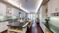 This well-appointed single-floor residence offers a refined living experience through a seamlessly connected open-concept layout. The kitchen is a standout, boasting crisp white shaker cabinetry, dark granite countertops, a green glass tile backsplash, and a full suite of stainless steel appliances including a gas range, built-in microwave, dishwasher, and French door refrigerator. A large central island with additional granite countertop space and open shelving doubles as a dining surface, anchored by elegant pendant globe lighting and ambient LED cove lighting overhead. Rich dark hardwood floors flow from the kitchen through to the dining and living areas, where French doors open to a private balcony, filling the space with natural light and offering views of the surrounding cityscape. The bedroom features plush carpeting, dual windows with urban views, and a ceiling fan, creating a calm and comfortable retreat. The en-suite bathroom includes a dual-sink vanity with dark countertops, large-format tile flooring, a soaking tub, and a glass-enclosed walk-in shower. A dedicated in-unit laundry room with a stacked washer and dryer and built-in shelving adds everyday convenience. Throughout, the space reflects a cohesive and polished design aesthetic.