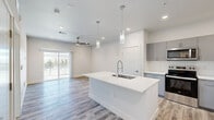 Located at 2830 Northtowne Ln in Reno, Nevada, this modern 1-bedroom, 1-bathroom unit offers a thoughtfully designed open-concept layout finished with light wood-look flooring and a crisp, neutral color palette throughout. The kitchen serves as the heart of the space, anchored by a large white quartz center island with an undermount sink and a professional-style pull-down faucet. Elegant pendant lighting hangs above the island, while gray shaker-style cabinetry, a white tile backsplash, and stainless steel appliances — including a range, microwave, and refrigerator — complete the contemporary kitchen design. The open living area flows seamlessly from the kitchen, featuring recessed lighting and a ceiling fan, and connects directly to a private balcony through sliding glass doors, allowing for abundant natural light and outdoor access. The spacious bedroom includes a ceiling fan, a window with blinds, and ample room for furnishings. The bathroom is cleanly finished with a combined tub and shower, a toilet, and matching wood-look flooring. Throughout the unit, the consistent modern finishes and clean lines create a cohesive, move-in-ready living environment.