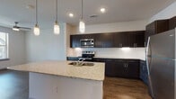 This well-appointed single-floor unit offers a thoughtfully designed open-concept layout with contemporary finishes throughout. The kitchen serves as the centerpiece of the living space, showcasing rich dark cabinetry, a classic white subway tile backsplash, and a full suite of stainless steel appliances including a range, microwave, and refrigerator. A spacious kitchen island with a granite countertop and integrated sink provides both additional prep space and a natural gathering point, illuminated overhead by stylish pendant lights. Durable wood-style flooring runs throughout the main living and kitchen areas, adding warmth and cohesion to the open floor plan.

The bedrooms offer a comfortable retreat, each featuring plush wall-to-wall carpeting and large windows dressed with blinds that invite natural light while offering privacy. A ceiling fan in the primary bedroom adds to the comfort of the space. The bathroom is finished with consistent dark cabinetry, granite countertops, a large vanity mirror, and a tiled tub-shower combination, complemented by wood-style flooring that ties back to the main living area.

Overall, the unit presents a clean, modern aesthetic with a cohesive design language carried through each room via matching cabinetry tones, granite surfaces, and contemporary fixtures.